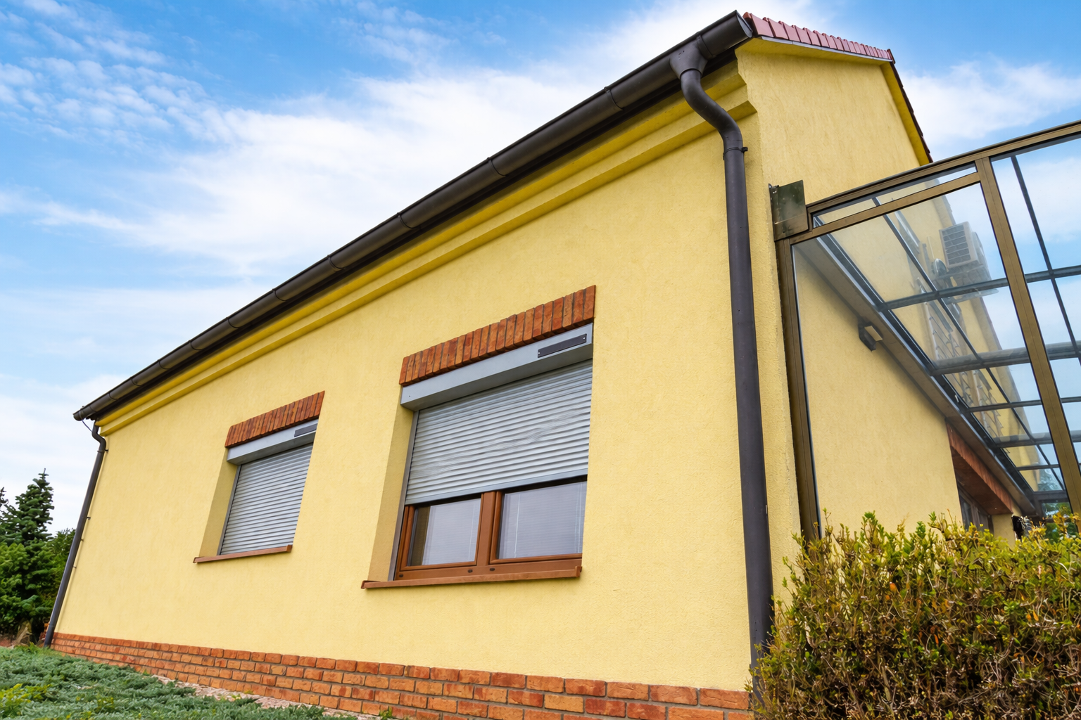 Detail fasády rodinného domu se dvěma venkovními roletami na oknech — stínění oken na solární pohon a chytré rolety bez zásahu do zdiva.